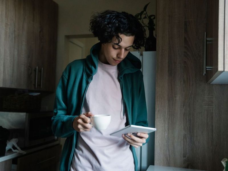 A man having a cup of tea while checking a tablet in the evening
