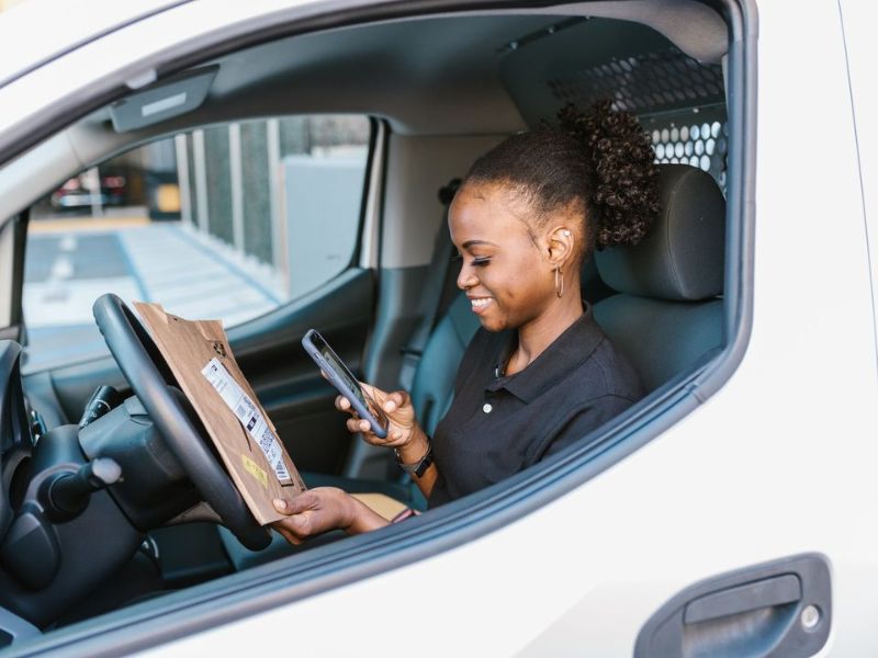 A tradesperson smiling at a phone notification from the driver's seat of a van