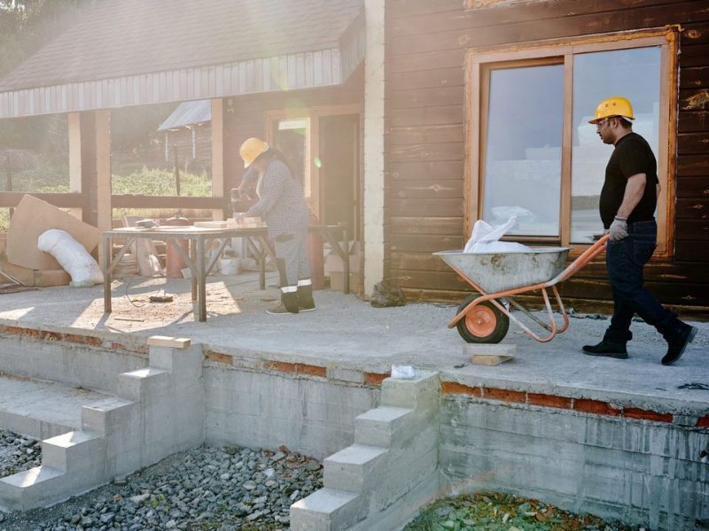 A tradesperson in a hard hat wheeling a barrow across a building site